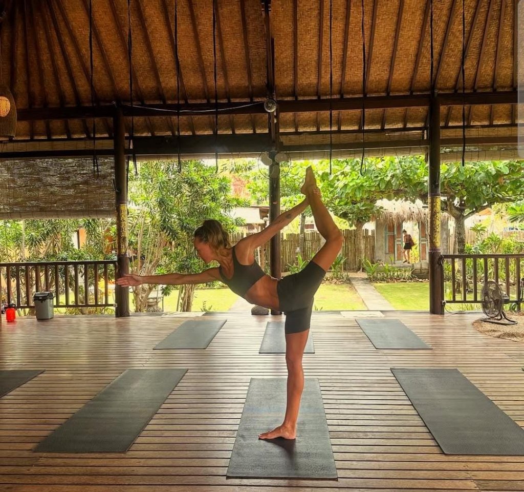 Group of people practicing yoga in Bali, surrounded by tropical greenery, with a peaceful wellness retreat atmosphere.