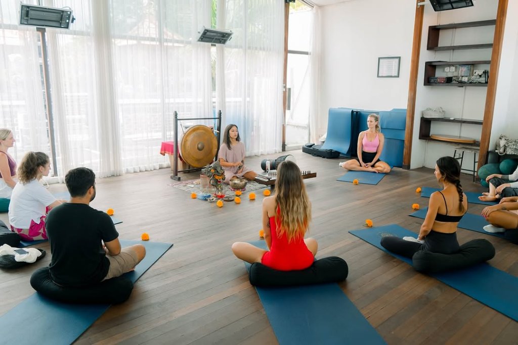 Participants engaging in sound healing and meditation in a tranquil tropical setting, using singing bowls and other instruments to promote relaxation and wellness.