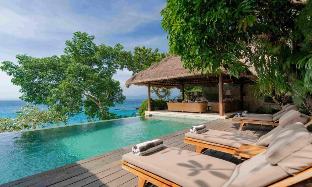 Spacious tropical villa named Villa Sayang Besar, featuring open-air living spaces, a large swimming pool, lush greenery, and traditional Balinese design elements